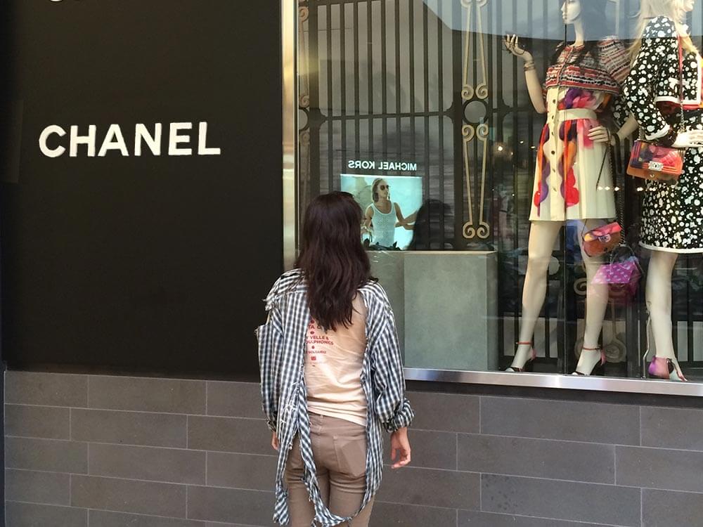 Teresita stands in front of a Chanel store wearing a torn, sun-damaged shirt.