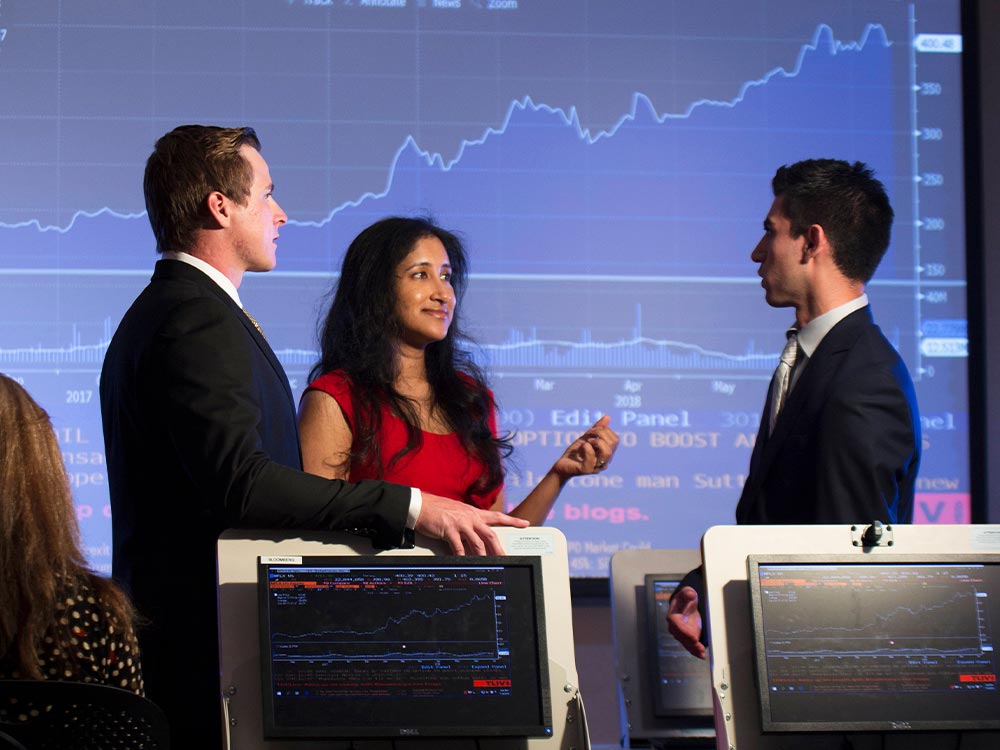 3 Titan Capital Management students stand in front of financial graph projection